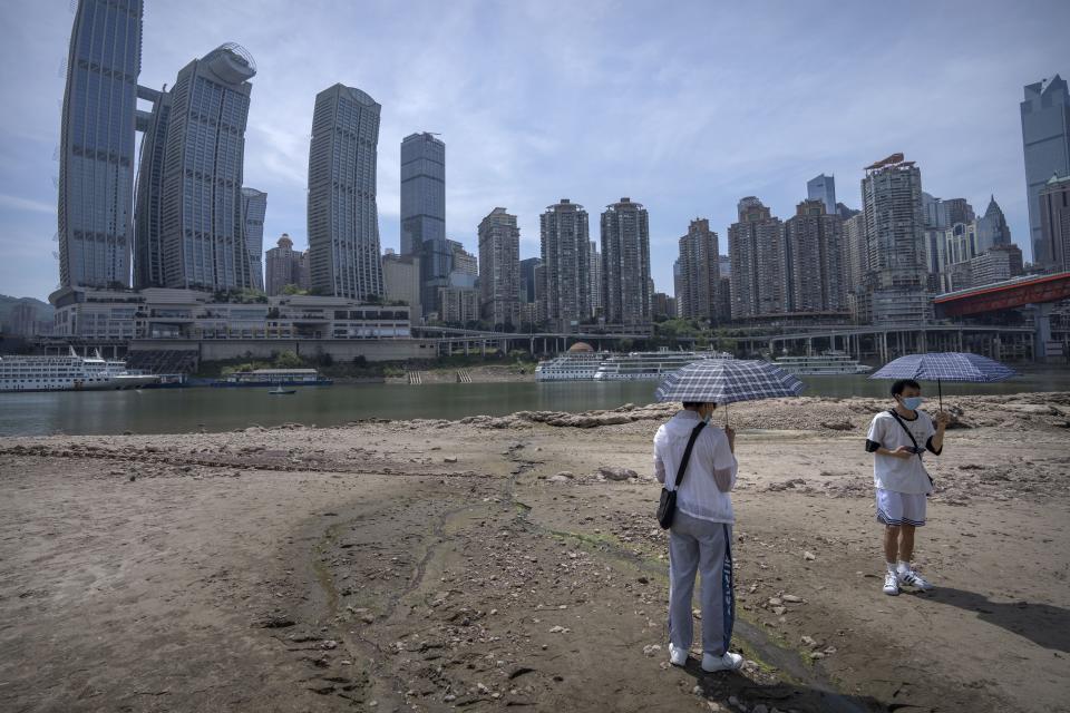 FILE - Students carrying umbrellas stand on the dry riverbed of the Jialing Rivera, a tributary of the Yangtze, in southwestern China's Chongqing Municipality, Aug. 19, 2022. A new study finds that climate change is making droughts faster and more furious. An expert says most of China’s Yangtze River basin last summer was struck by a flash drought that developed within only a month due to high temperatures. (AP Photo/Mark Schiefelbein, File)