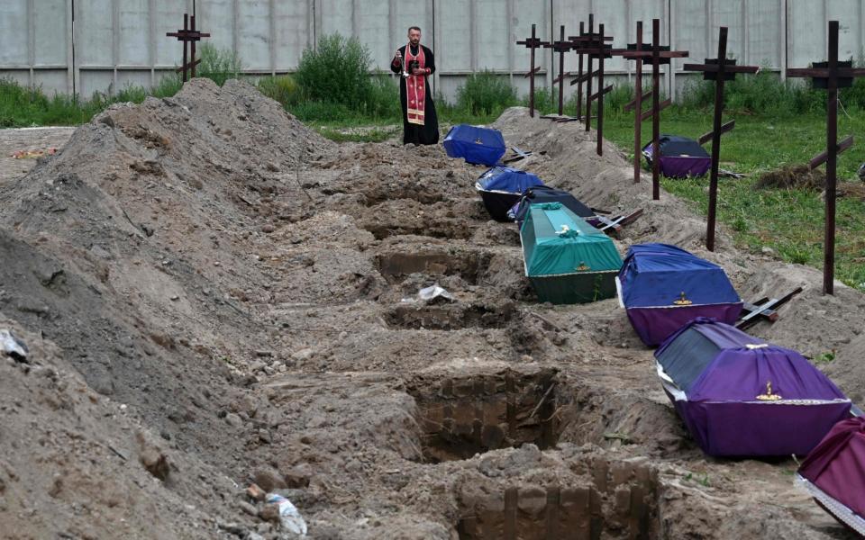An Orthodox priest prays at the graves of unidentified civilians during their funeral at a local cemetery in the city of Bucha, Kyiv region, on Thursday - ERGEI SUPINSKY/AFP 