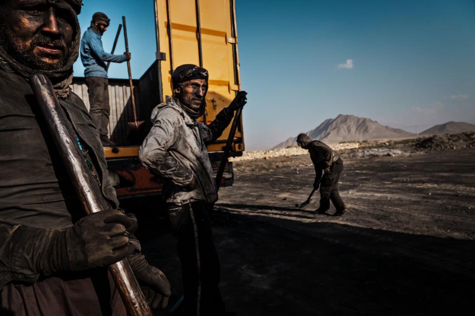 A group of men finish shoveling coal into transport trucks