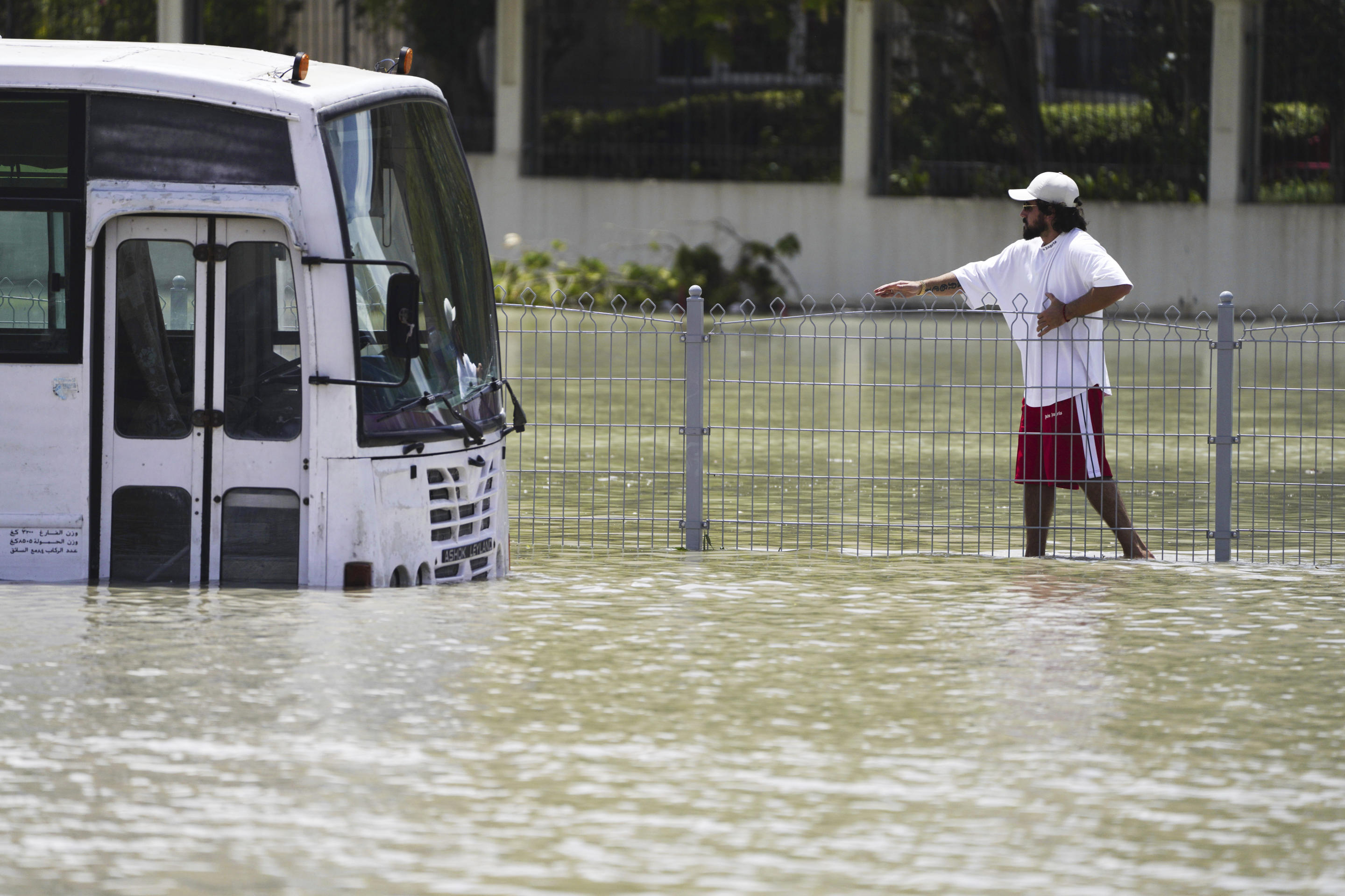 A man clings to a fence as he walks through floodwaters in Dubai.