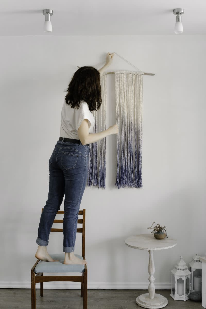 A woman hangs a decorative piece on the wall of her home