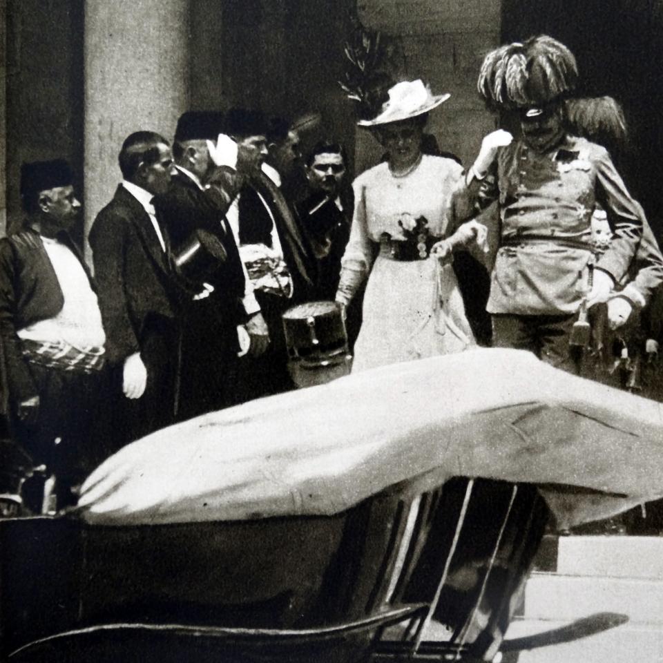 Archduke Franz Ferdinand and his wife Sophie, Duchess of Hohenberg, walk towards a car, surrounded by men in traditional and military attire