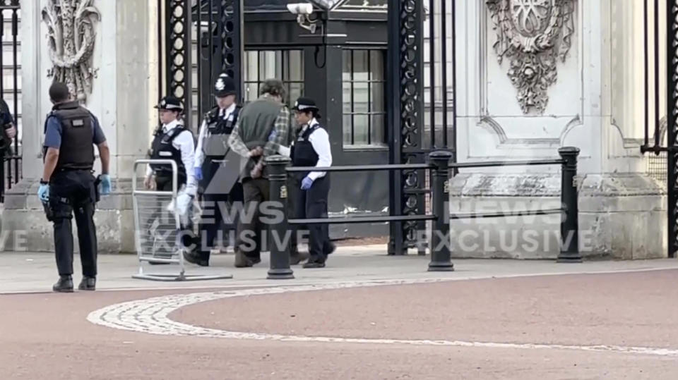 This image from a video shows police surrounding a man outside Buckingham Palace gate in London, Tuesday, May 2, 2023. London police said a controlled explosion was carried out as a precaution outside Buckingham Palace late Tuesday after a man was arrested there on suspicion of possessing an offensive weapon. (CHANNEL 7 via AP)