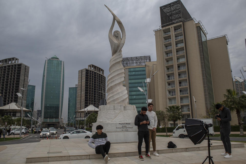 People stand by a monument in Irbil, Iraq, Tuesday, March 21, 2023. The Kurdish in Iraq region won de facto self-rule in 1991 when the United States imposed a no-fly zone over it in response to Saddam's brutal repression of Kurdish uprisings. With American invasion 20 years ago much of Iraq fell into chaos, as occupying American forces fought an insurgency and as multiple political and sectarian communities vied to fill the power vacuum left in Baghdad. But the Kurds, seen as staunch allies of the Americans, strengthened their political position and courted foreign investments. (AP Photo/Hawre Khalid, Metrography)