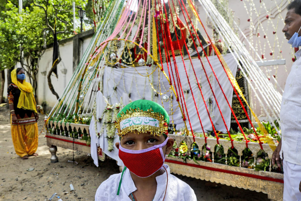 A Muslim boy wearing face mask stands in front of a replica of the highest seat of Imam Hussain, the great grandson of Prophet Muhammad prior to a Muharram procession in Kolkata, India, Sunday, Aug. 30, 2020. India has the third-highest coronavirus caseload after the United States and Brazil, and the fourth-highest death toll in the world. (AP Photo/Bikas Das)