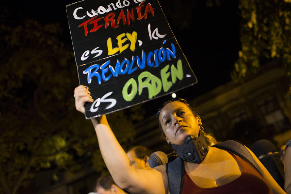 A woman holds a sign with message that reads in Spanish: "When tyranny is the law, a revolution is in order" during a protest outside the governor’s residence, the Fortaleza, after Pedro Pierluisi was sworn in as Puerto Rico's governor, in San Juan, Puerto Rico, Friday, Aug. 2, 2019. Departing Puerto Rico Gov. Ricardo Rossello resigned as promised on Friday and swore in Pierluisi, a veteran politician as his replacement, a move certain to throw the U.S. territory into a period of political chaos that will be fought out in court. (AP Photo/Dennis M. Rivera Pichardo)