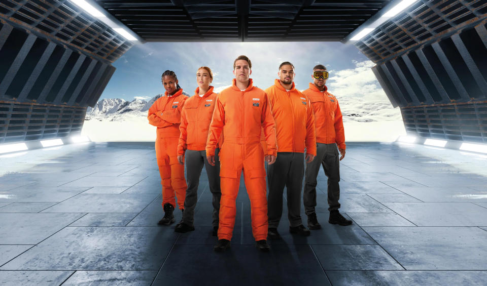 Five people standing in a V wearing orange Columbia Star Wars Luke Skywalker pilot gear against the open door of a star ship with snow behind