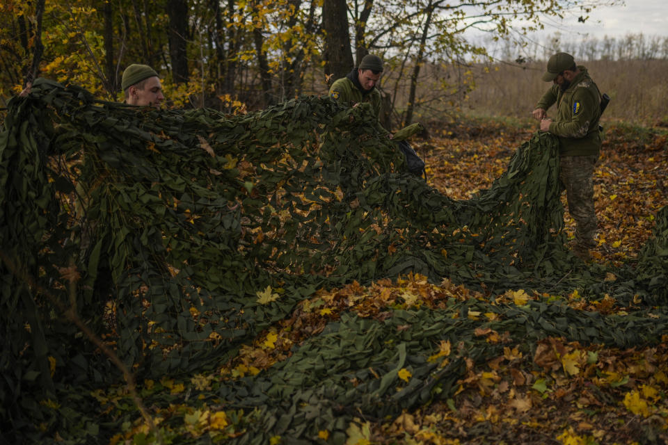 Desminadores de las fuerzas de defensa territorial de Ucrania retiran una red de camuflaje, que reutilizarán, en un campamento militar ruso abandonado cerca de Hrakove, Ucrania, el 13 de octubre de 2022. (AP Foto/Francisco Seco)