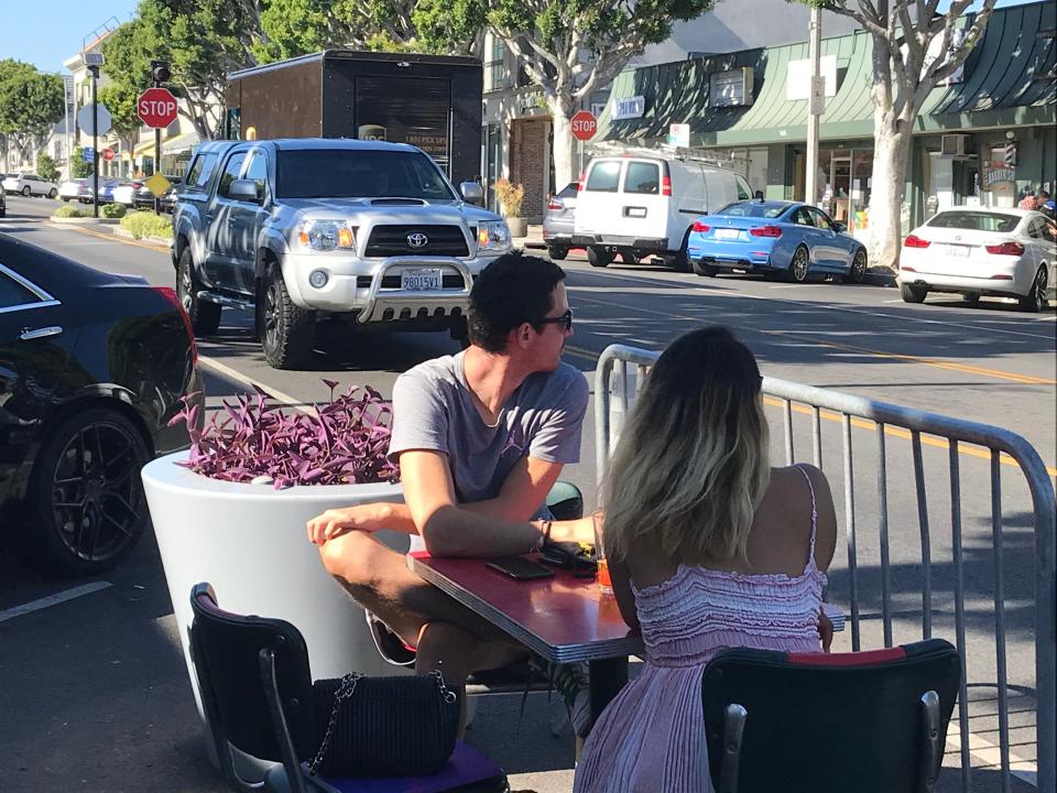 A pair of diners sit at a restaurant table in the street on  Larchmont Boulevard section of Los Angeles, separated from traffic by only a metal fence and protected by only a planter