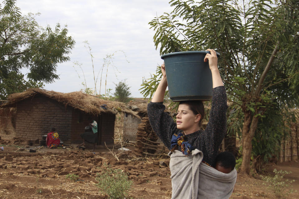 Cameron Beach, carries a carries a bucket of water on her head collected from a communal borehole in Dedza, near Lilongwe, Malawi, Friday, July 23, 2021. Beach, a former Peace Corps volunteer, is living in rural Malawi teaching English at a rural high school where she had been sent by the United States government 18-months before COVID-19 began sweeping the world. (AP Photo/Roy Nkosi)