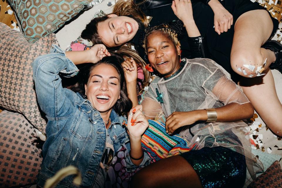 happy smiling girlfriends relaxing on floor with cushions and confetti