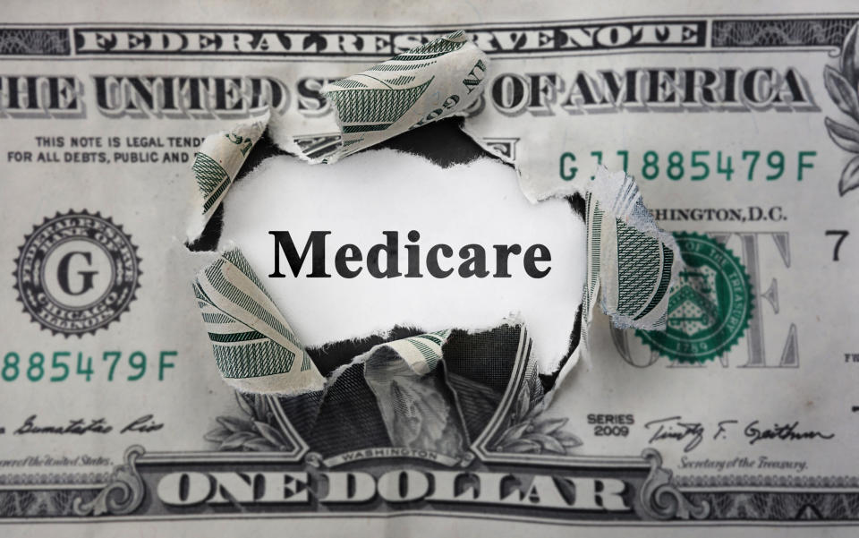 Torn one dollar bill with the word "Medicare" showing through the hole.