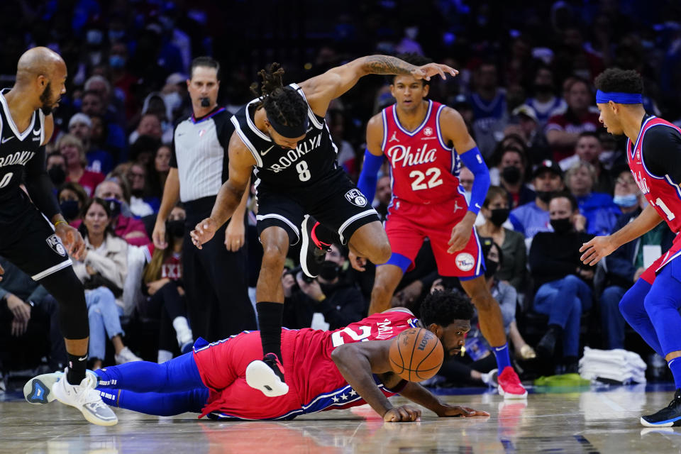 Brooklyn Nets' Patty Mills (8) leaps over Philadelphia 76ers' Joel Embiid (21) during the first half of an NBA basketball game, Friday, Oct. 22, 2021, in Philadelphia. (AP Photo/Matt Slocum)