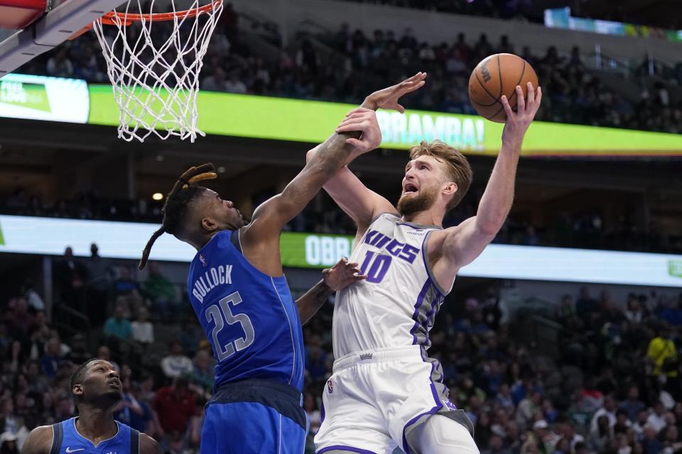 Dallas Mavericks forward Reggie Bullock (25) defends as Sacramento Kings forward Domantas Sabonis (10) leaps to the basket for a shot in the second half of an NBA basketball game in Dallas, Saturday, March, 5, 2022. (AP Photo/Tony Gutierrez)