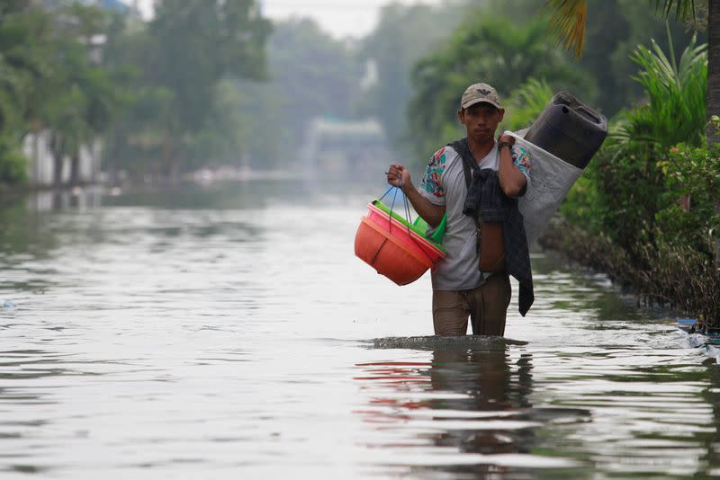 A man carries baskets through a flooded road, at an area affected by land subsidence and rising sea level in North Jakarta