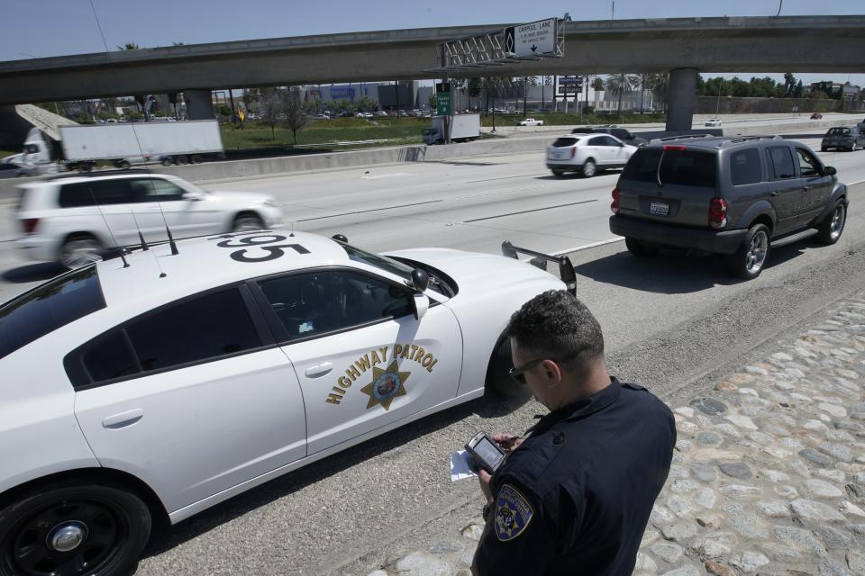 FILE - In this April 23, 2021 file photo, California Highway Patrol officer Troy Christensen runs a driver's license after stopping a motorist along Interstate 5 who was suspected of speeding in Anaheim, Calif. The number of highway deaths in 2020 was the greatest in more than a decade even though cars and trucks drove fewer miles during the pandemic, and motorists are continuing to speed, tailgate and zigzag through traffic. (AP Photo/Chris Carlson)