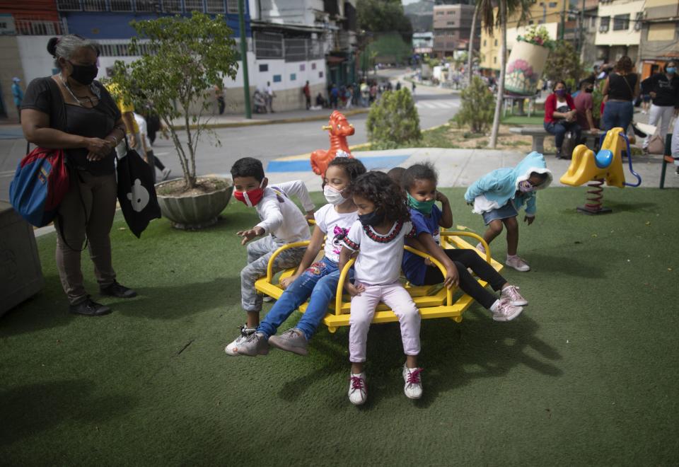 Children wearing protective face masks ride a merry go round in a park in Caracas, Venezuela, Friday, July 17, 2020, amid the new coronavirus pandemic. (AP Photo/Ariana Cubillos)