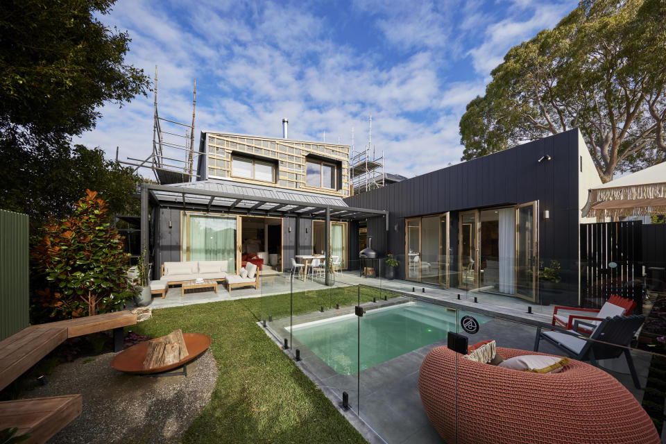 A wide shot of the backyard with the pool on the right, a seating area on the left and a concrete area at the back. 