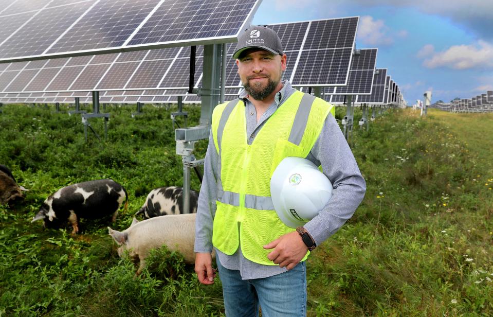 Caleb Scott, a farmer and entrepreneur, with some of his livestock that feed in a solar field in Lansing, New York. The Kunekune pigs and number of sheep roam the area feeding on nutritious grasses under the solar panels.