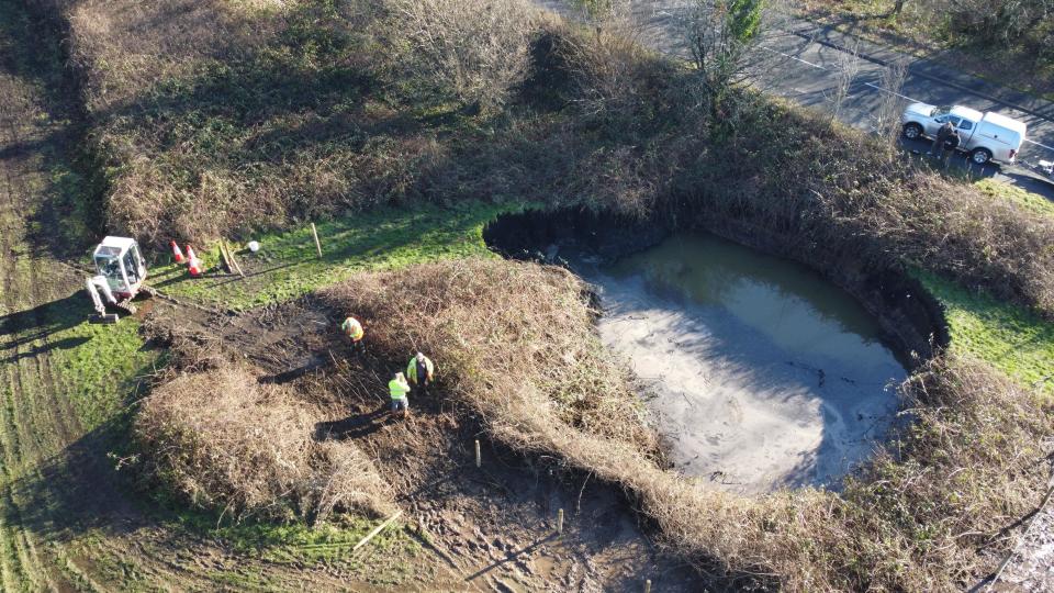 A huge sinkhole next to a busy road is cordoned off with a fence. 