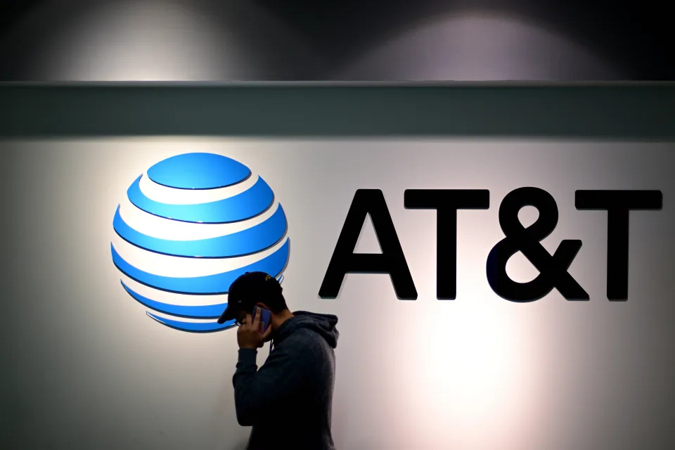 A man holds a phone to his ear while walking past an AT&T sign.