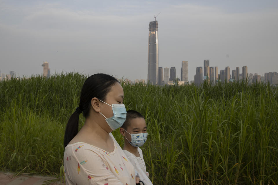 In this April 16, 2020, photo, residents wearing masks against the coronavirus walk past reeds and the cityscape along the Yangtze River in Wuhan in central China's Hubei province. Wuhan has been eclipsed by Shanghai, Hong Kong and other coastal cities since the ruling Communist Party set off a trade boom by launching market-style economic reforms in 1979. But for centuries before that, the city was one of the most important centers of an inland network of river trade that dominated China's economy and politics. (AP Photo/Ng Han Guan)