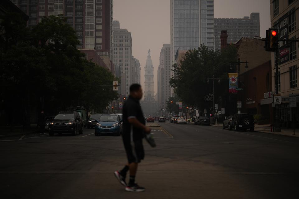 FILE - A man crosses Broad Street past a hazy City Hall, June 7, 2023, in Philadelphia. Thick, smoky air from Canadian wildfires made for days of misery in New York City and across the U.S. Northeast this week. But for much of the rest of the world, breathing dangerously polluted air is an inescapable fact of life — and death. (AP Photo/Matt Slocum, File)
