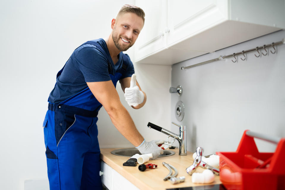 Happy Young Male Plumber Fixing Faucet In Kitchen