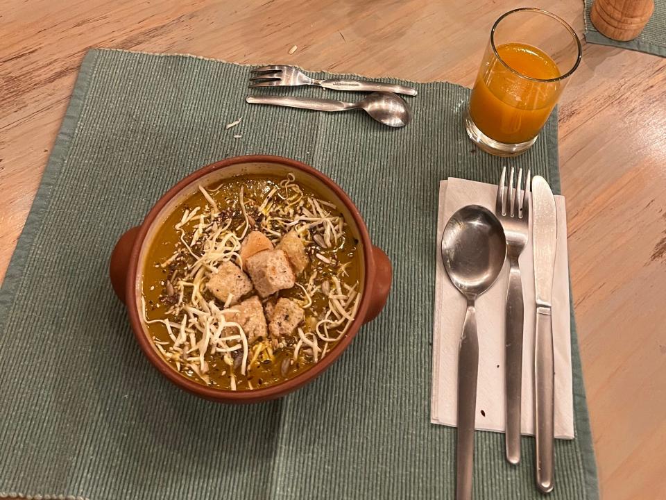 A bowl of soup and silverware on a teal placemat.