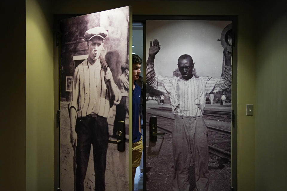 A person walks out as pictures from the Tulsa Race Massacre adorn doors leading to a prayer room dedicated to the massacre at the First Baptist Tulsa church during centennial commemorations, Sunday, May 30, 2021, in Tulsa, Okla. The church made the room to provide a place to explore the history of the Tulsa Race Massacre of 1921 and to prayerfully oppose racism. (AP Photo/John Locher)