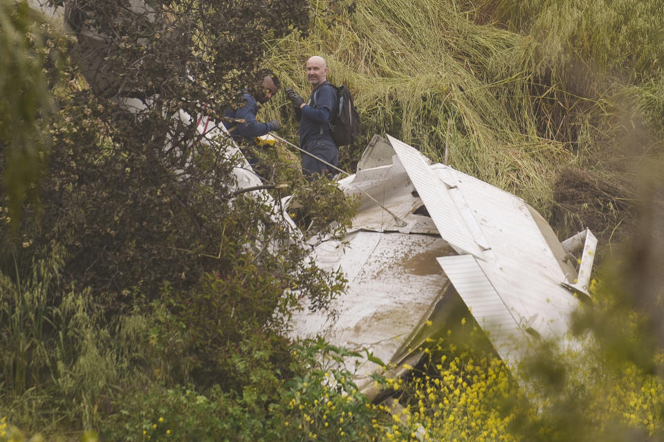 National Transportation Safety Board investigators inspect a downed plane on a steep hill above a home on Beverly Glen Circle in Los Angeles, Sunday, April 30, 2023. Fire department officials said a person was found dead following an intensive search for the single-engine airplane that crashed in a foggy area Saturday night. (AP Photo/Damian Dovarganes)