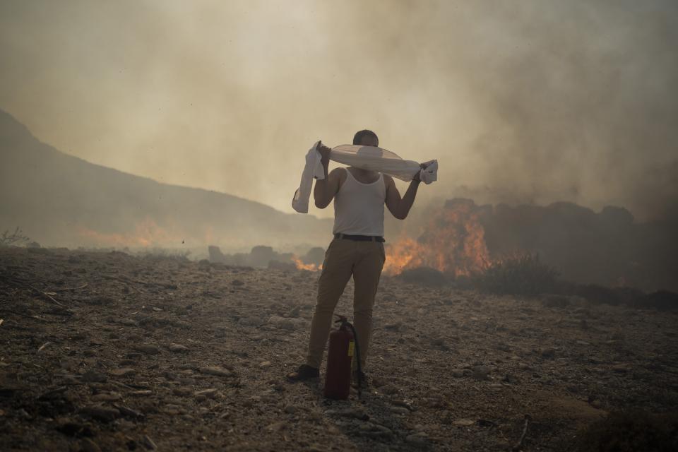 Ein Mann wickelt ein Handtuch um seinen Kopf, während er versucht ein Feuer in der Nähe des Badeortes Lindos auf der Insel Rhodos zu löschen. (Bild: Petros Giannakouris/AP/dpa)