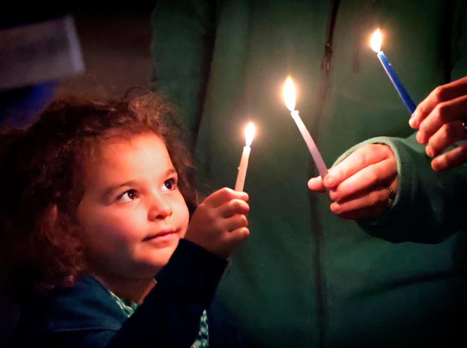 Four-year-old Riley Gillet, of Orlando, lights a candle with her family, marking the beginning of the traditional Jewish holiday of Hanukkah, during the Chabad of Greater Orlando's "Chanukah on the Park" celebration in Winter Park, Fla., late Sunday, Nov. 28, 2021. Held at Central Park, the event included the lighting of a giant menorah, live performers, music and dancing.