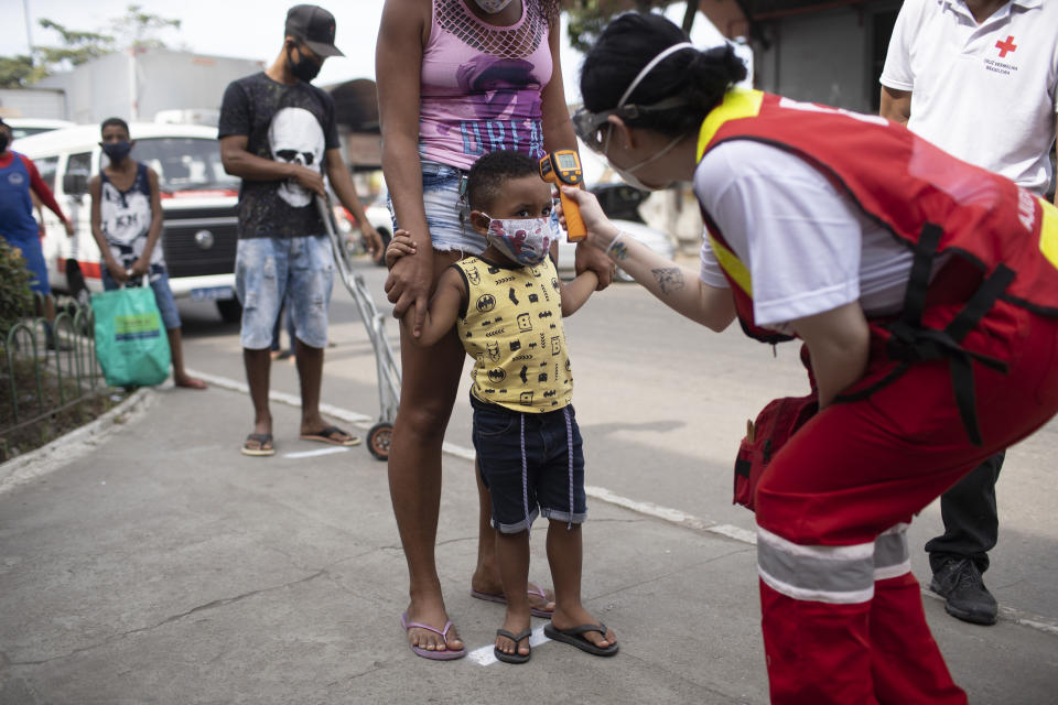 A member of the Red Cross checks the temperature of a child at the CEASA, Rio de Janeiro's main wholesale market, amid the new coronavirus pandemic in Rio de Janeiro, Brazil, Tuesday, June 23, 2020. Many markets that were initially closed have reopened with health measures like limiting the number of people, forming orderly lines, taking temperatures and requiring the use of masks. (AP Photo/Silvia Izquierdo)