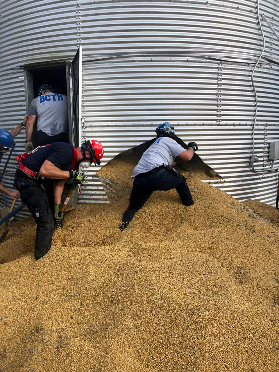 In this May 30, 2019 photo provided by the Ross Township Fire Department rescue personnel shovel soybeans out of the bottom of a bin during an effort to rescue farmer Jay Butterfield, who was buried up to his neck inside. He became buried up to his neck while trying to break up clumps of soybeans in the bin on his farm in Ross Township, Ohio. (Ross Township Fire Department via AP)