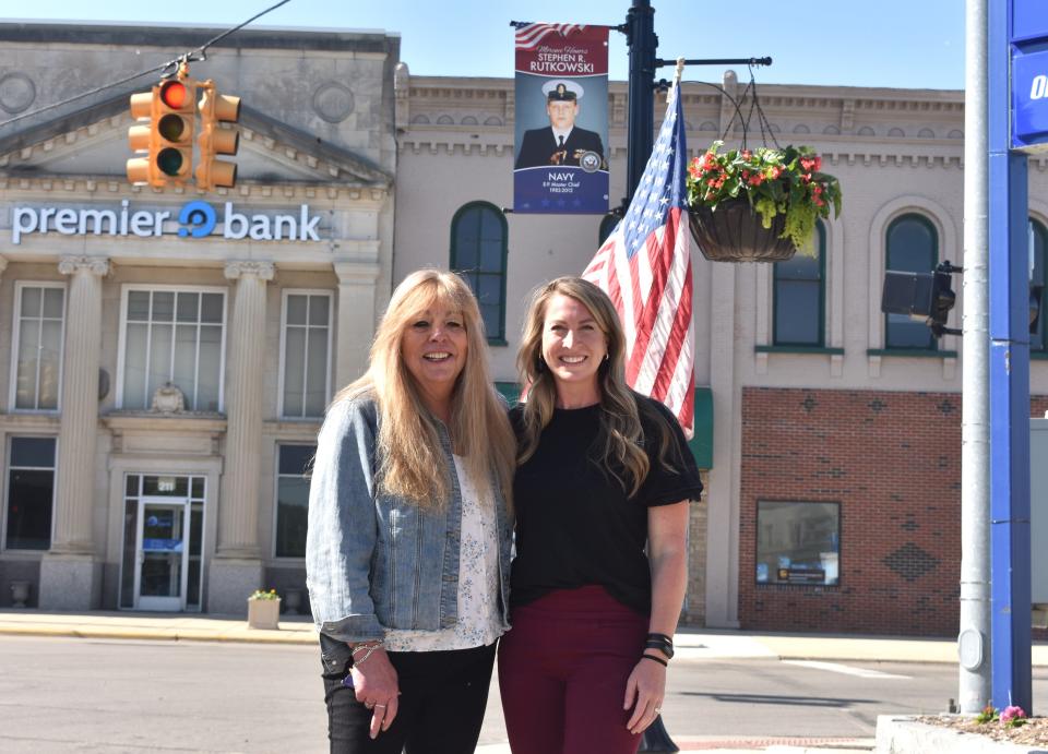 Chris Rutkowski, left, and Heather Sarnac, right, the community and economic development director for the city of Morenci, are pictured Thursday near the Hometown Heroes banner of Rutkowski's husband, Stephen Rutkowski, a 30-year sailor in the United States Navy.