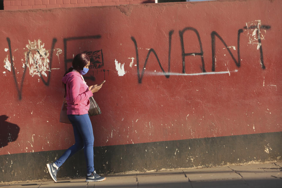 A woman uses her mobile phone while walking past a wall with graffiti on the streets of Harare, in this Tuesday, July 7, 15, 2020 photo. Unable to protest on the streets, some in Zimbabwe are calling themselves "keyboard warriors" as they take to graffiti and social media to pressure a government that promised reform but is now accused of gross human rights abuses.(AP Photo/Tsvangirayi Mukwazhi)