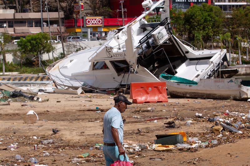 Un hombre camina cerca de un barco dañado entre escombros en la playa tras el paso del huracán Otis, en Acapulco