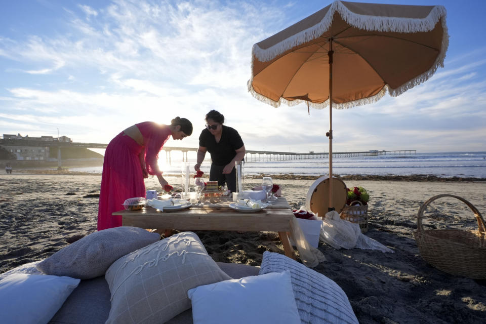 Isabela, left, and Diana Kihara set up a table for two for a couple to watch the sun dip below the Ocean Beach pier, behind, at sunset, Tuesday, Jan. 30, 2024, in San Diego. The Kihara Rising seas, frequent storms take toll on California's iconic piers, threatening beach landmarks (AP Photo/Gregory Bull)