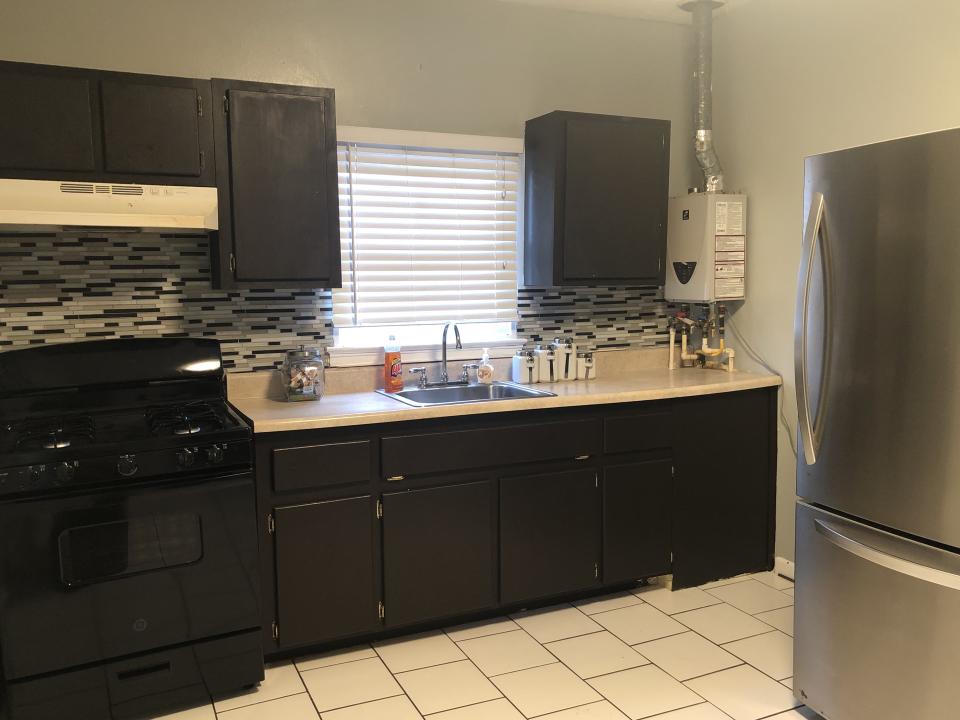 Modern kitchen with a gas stove, stainless steel refrigerator, tiled backsplash, and window with blinds over the sink