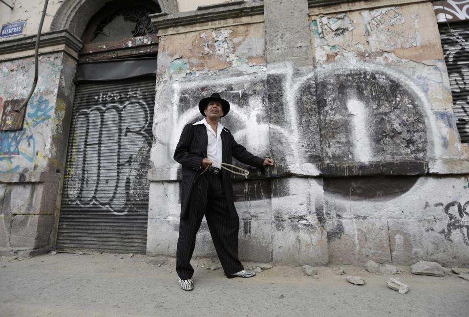 Flores Mujica wears his "Pachuco" outfit while posing for a photograph next to a wall with graffiti in Mexico City