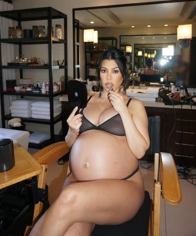 <p>Kourtney Kardashian Instagram</p> Kourtney Kardashian puts on lipgloss as she bares her growing bump