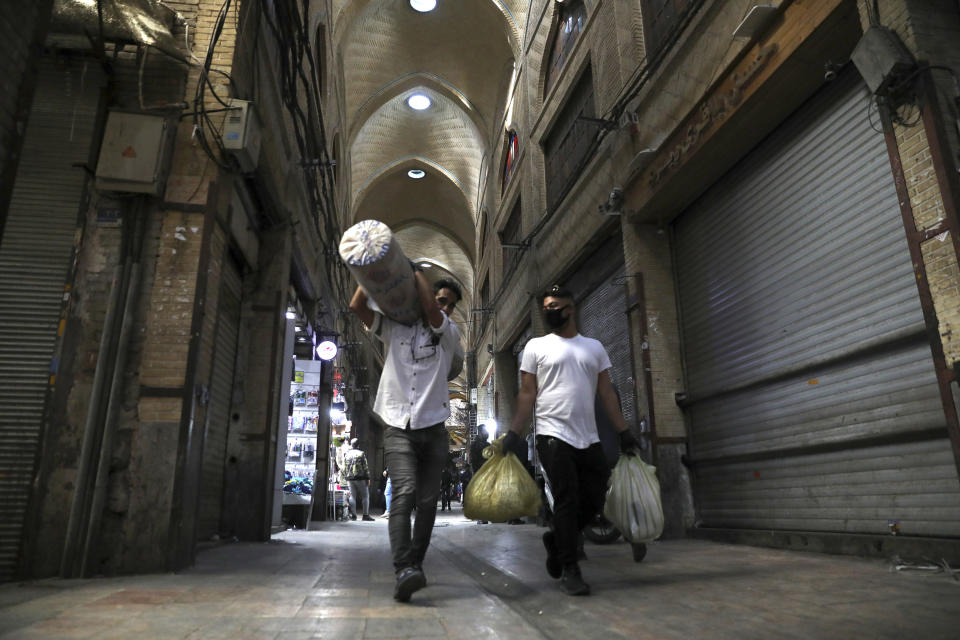 In this Tuesday, March 17, 2020, photo, men carry their goods through mostly closed Tehran's Grand Bazaar, Iran. The new coronavirus ravaging Iran is cutting into celebrations marking the Persian New Year, known as Nowruz. (AP Photo/Vahid Salemi)