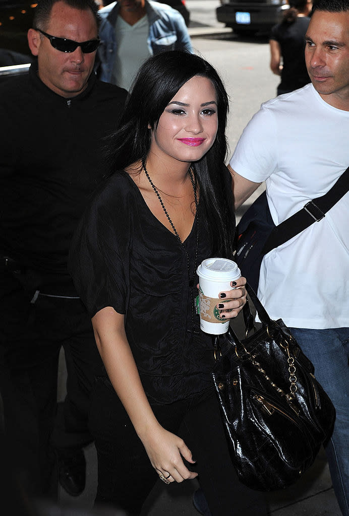 Demi walking outside holding a coffee from Starbucks