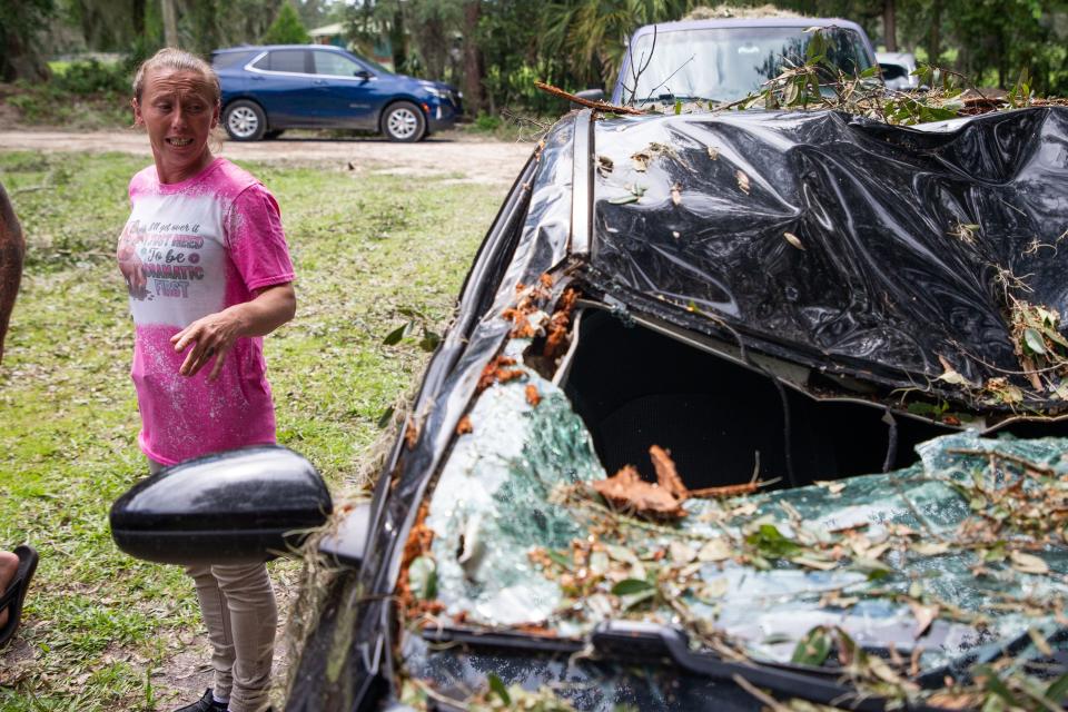 Jessica Shyer stands by her car that was crushed by an oak tree, estimated to be 80 feet tall, during Hurricane Idalia in Cross City, Fla. on Thursday, Aug. 31, 2023.
