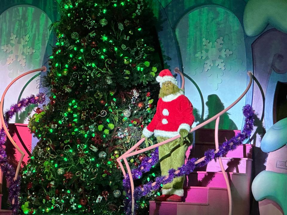 Person in Grinch costume on steps at universal studios in front of a large Christmas tree