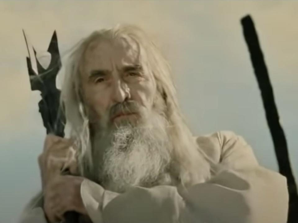 Saruman in white holding a staff in lord of the rings