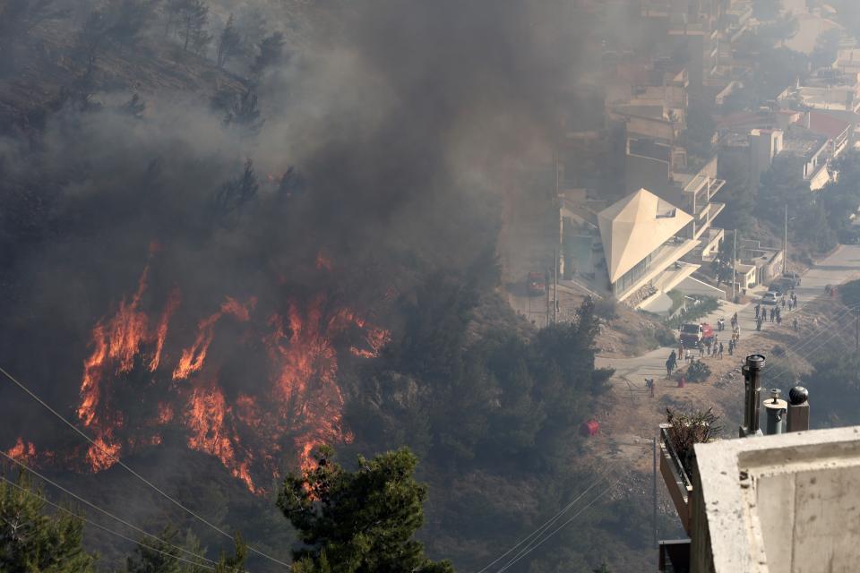 Flames burn trees on a hill as people look on during a wildfire in Voula suburb, in southern Athens, Greece, Saturday, June 4, 2022. A combination of hot, dry weather and strong winds makes Greece vulnerable to wildfire outbreaks every summer. (AP Photo/Yorgos Karahalis)