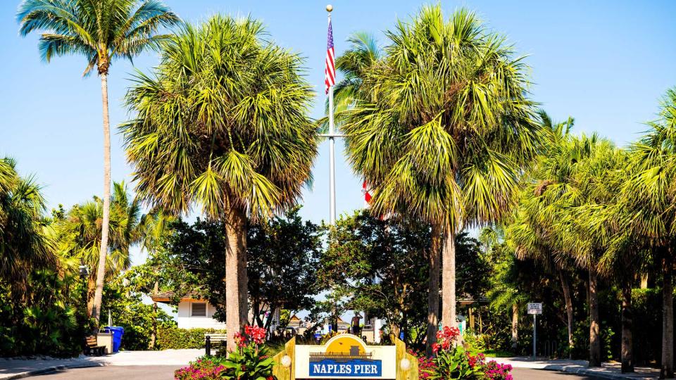 Naples pier, Florida entrance sign with palm trees and American flag on flagpole in wealthy neighborhood community