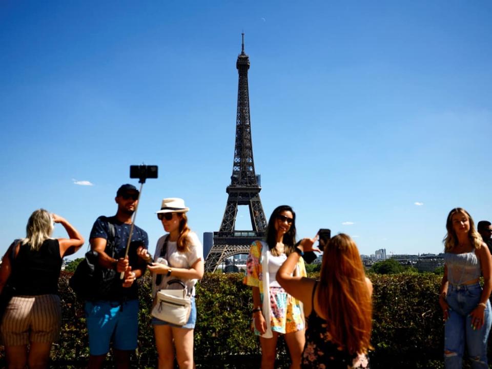 Tourists pose for pictures in Paris, with the Eiffel Tower in the background, in early August 2022. Europe has seen multiple waves of sweltering heat this summer, part of the reason travel industry experts say the shifting climate has the potential to change travel-timing habits.  (Sarah Meyssonnier/Reuters - image credit)